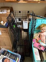 Full view of rectangular black wire mesh live animal trap sized for groundhogs, with visible door mechanism and surrounding miscellaneous items.