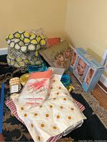 Photo showing assorted linens and pillows including daisy patterned pillow sham, embroidered quilted throw, and various decorative pillows.