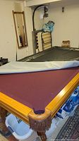 Pool table with grey cover partially pulled back showing burgundy felt playing surface and wood frame.