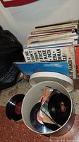 Photo of vintage vinyl records stacked and in a canister showing some 45 RPM records and various album covers.