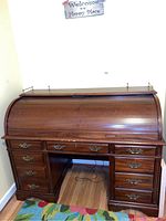 Front view of wooden roll top desk showing curved tambour top and nine drawers