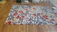 Full view of the rectangular area rug showing overall floral and abstract pattern and color scheme on wooden floor.