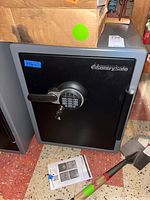 Full front view of black Sentry Safe with digital keypad, handle, and instructions on the floor nearby.