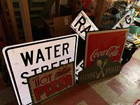 Photo showing the full set of metal signs including Water Street, Hot Italian Pizza, Coca-Cola, Good Food plaque, and railroad crossing sign.
