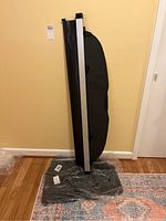 Black retractable trunk blind with aluminum support rail leaning against wall, Subaru Outback model.