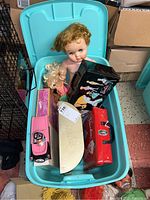 Overall view of turquoise plastic container holding vintage Barbie dolls, carry cases, lunch boxes, and accessories.