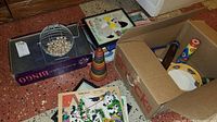 Wide view of vintage bingo cage on Monte Carlo box, wooden puzzles, stacking rings, tambourine, and kaleidoscope toy, with some items packed in a cardboard box.