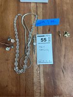 Full view of all jewelry items including the clear beaded necklace with silver extension, 14K gold monogrammed pin, sterling silver sword pin, heart-shaped pendants and stud earrings.