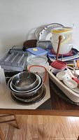 Wide view of stacked mixing bowls, Pyrex dishes, Rubbermaid containers, and kitchen trays including aluminum trays and a gold-tone tray. Various lids and kitchen tools visible.