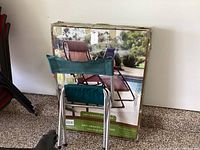 Photo of item folded in front of original packaging box showing the chair and the box printing with chair image and product details.