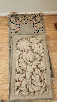 Two handmade wool area rugs stacked, showing floral patterns and fringe on the rug beneath.