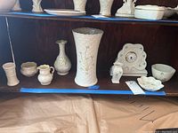 Shelf display of Belleek pottery items including vases, pitcher, dish, and clock with shamrock motifs.