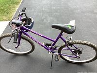 Side view of purple Rallys women's bike showing frame, seat, tires, and handlebar with front light and attached helmet.
