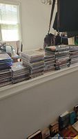 Stacks of CDs and DVDs on a railing by a window in natural light