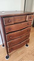 Frontal view showing six dovetailed drawers with wooden knobs and keyholes, curved drawer fronts, and slight damage or wear spots on the left side.