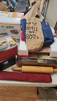 Items on table including boxed Rival Crock-Pot, wine tote bag, wooden rolling pin, aprons, wrist rest