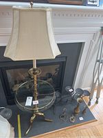 Full view of brass floor lamp with glass table top, several metal candle holders, and two vases arranged near a fireplace.