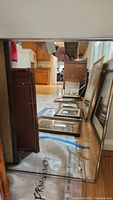 Large rectangular mirror with carved wood frame reflecting hardwood floors and framed pictures, showing size and condition