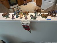 Full view of all 15 hand painted nativity figures and animals arranged on a flat surface including human characters, animals, and a mini nativity scene.