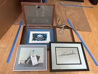 Lot of navy art and memorabilia items including framed prints, etched glass bell, and empty frames on wooden floor