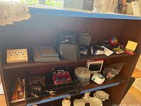 Wide view of wooden shelves holding locks, measuring tapes, a timer, CD spindle, pencil sharpener, and assortment of other office supplies and small household items.