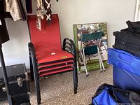 Four stacked patio chairs with red fabric seats and black metal frames shown in a garage setting.