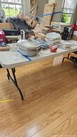 Full view of the plastic folding table with various other household items on top, showing table size and general condition.