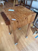 Full view of rolling butcher block table showing square hollow butcher block top and wooden legs with wheels.