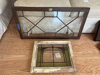 Photo of a wood-framed glass door with latch and hinges, placed on a wooden floor in front of a couch.