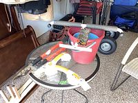 Wide angle photo showing white storage hook, red Corona pruning clipper, glass lifter, and buckets placed on a round glass table.