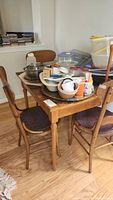 Side view of table with various household items on top, showing fluted legs and wooden chairs
