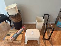 Four trash cans stacked: tall black wicker, medium brown wicker, white round plastic, and white rectangular plastic. White step stool and wooden wine box visible.