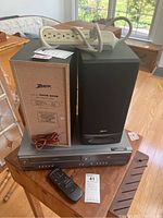 Magnavox VHS/DVD player with Zenith speakers on top, white RCA power strip coiled on top, black remote control placed in front.