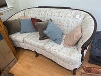 Full view of floral upholstered curved sofa with dark carved wood frame and six assorted throw pillows in front.