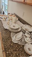 Photo showing full spread of Winterling Schwarzenbach china including plates, cups, mugs, and serving bowls laid out on countertop.