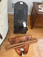 Front view of dark carved wood chair with metal embossed decoration on the backrest. Triangle leather seat and wooden tripod legs visible below.