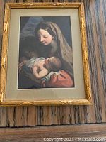 Framed print of Madonna holding infant wrapped in cloth, light colored mat with wooden frame.