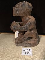 Side angled view of wooden African monkey figure showing shape and texture, placed on beige fabric.