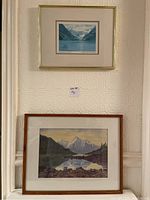 Photo shows two framed pieces hung on a patterned cream wall, one above the other. The top is a smaller print in a gold frame, and the bottom is a larger watercolour painting in a wooden frame.