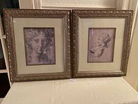 Two framed prints on a table, showing classical style portraits with ornate frames and embossed mats.