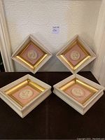 Four square framed artworks each with a white medallion on pink velvet, arranged in diamond and square orientations showing overall lot setup.