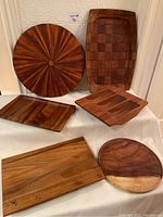 Photo of seven assorted teak and wooden serving trays and bowls arranged on a white cloth, showing various shapes and wood grains.