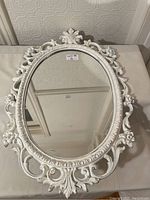 Ornate white oval mirror front view showing detailed carved floral and scroll design frame.