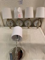 Five wall sconces displayed on a table: one larger chrome Generation sconce in box and four smaller brass-colored sconces with fabric shades.