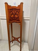 Front view of vintage wooden plant stand with carved decorative panels and tapered legs