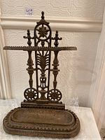 Front view of the heavy metal umbrella stand showing detailed Victorian-inspired design and the tray base.