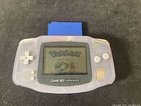 Game Boy Advance handheld console powered on displaying Pokémon Blue Version start screen with blue cartridge inserted, showing console functionality.