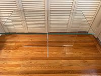 Front and top view of clear acrylic table with thick glass top, placed on wooden floor and in front of white louver doors.