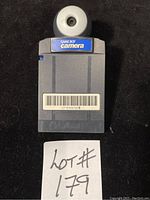 Front side of the GameBoy Camera showing the gray cartridge with the round camera lens and GameBoy Camera label.