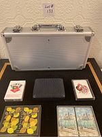 Closed silver metal carrying case with poker chips and five decks of cards placed in front